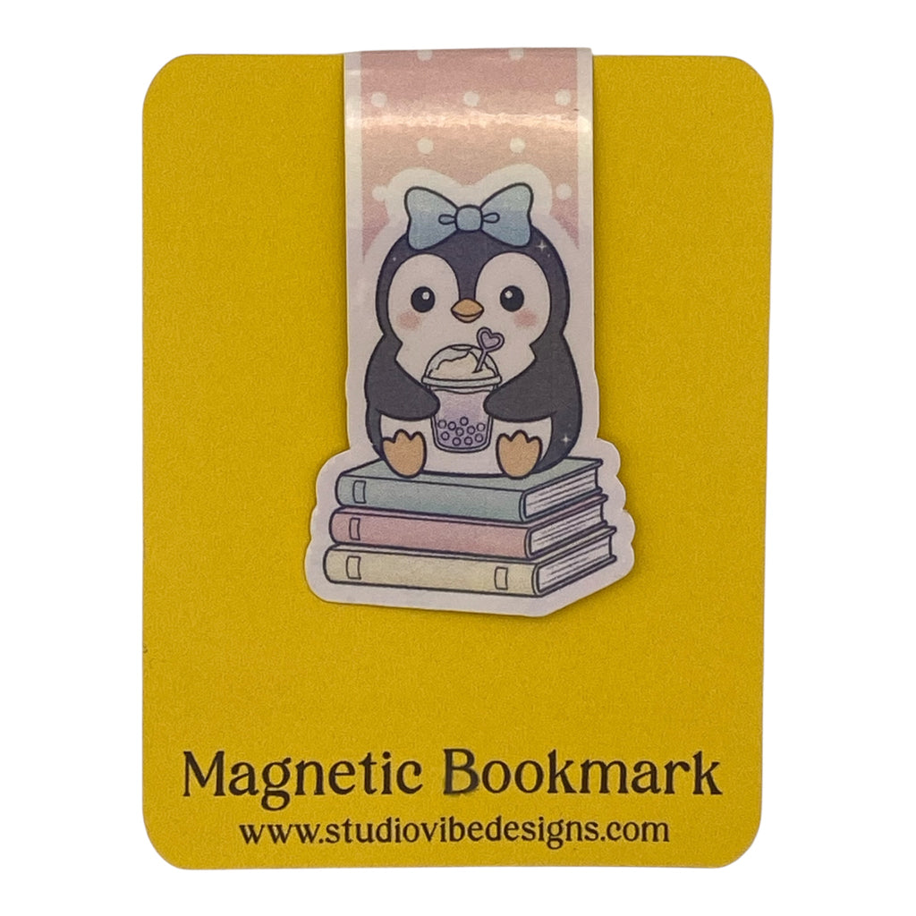 A yellow magnetic bookmark card featuring a cute cartoon penguin sitting on stacked books with a pink bow. The card reads 'Magnetic Bookmark' and shows the website 'www.