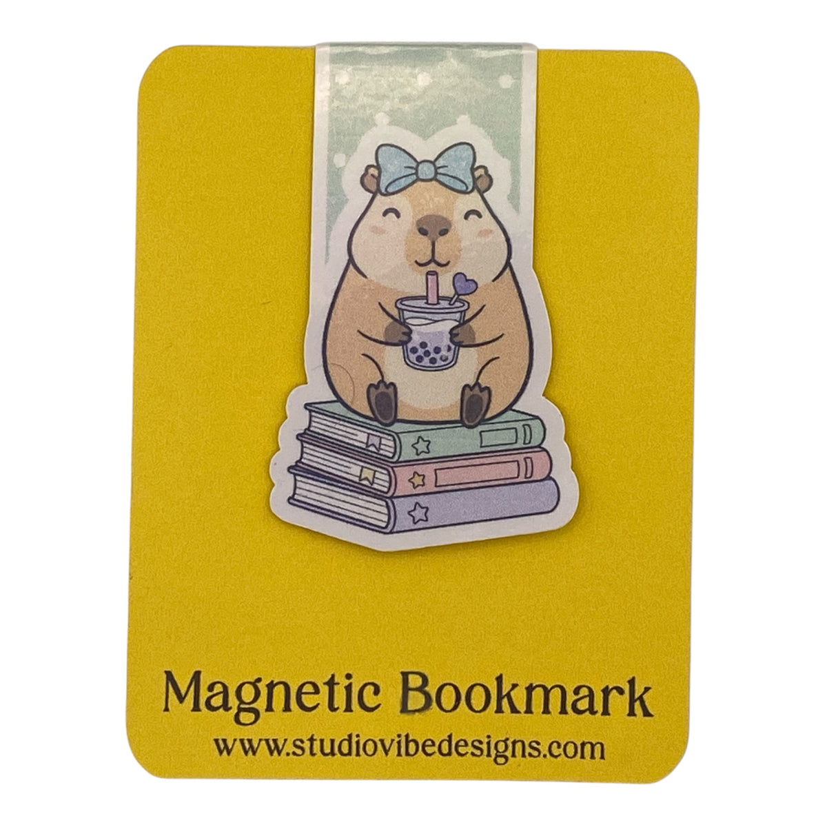 A cute cartoon beaver holding a bubble tea on a stack of books, mounted on a yellow magnetic bookmark card with the text 'Magnetic Bookmark' and 'www.studiovidesigns.