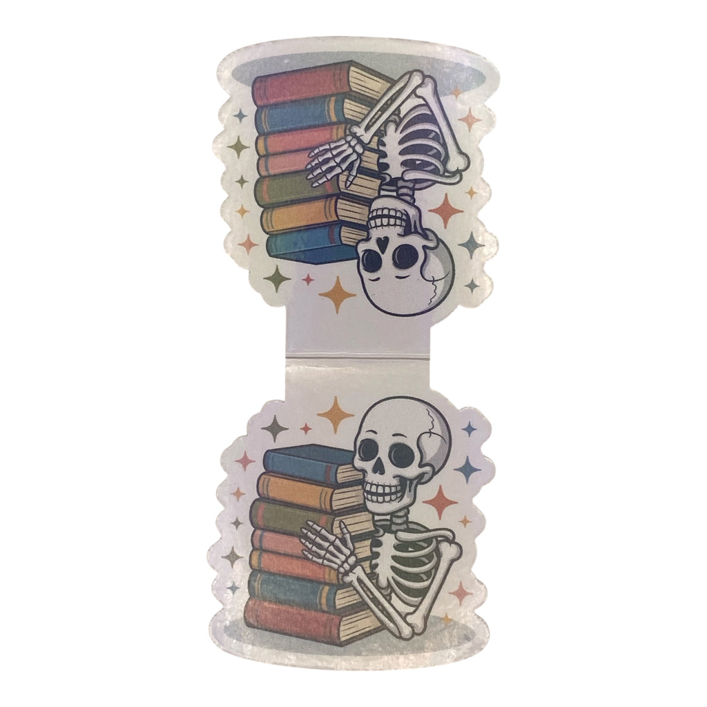 A die-cut magnetic bookmark featuring a cartoon skeleton holding a stack of colorful books, with a smaller skull detail and star accents, shown on a plain white background.
