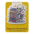 A yellow magnetic bookmark card featuring a die-cut illustration of a cartoon skeleton holding a stack of books, with the text 'Magnetic Bookmark' and 'www.studiovibedesigns.