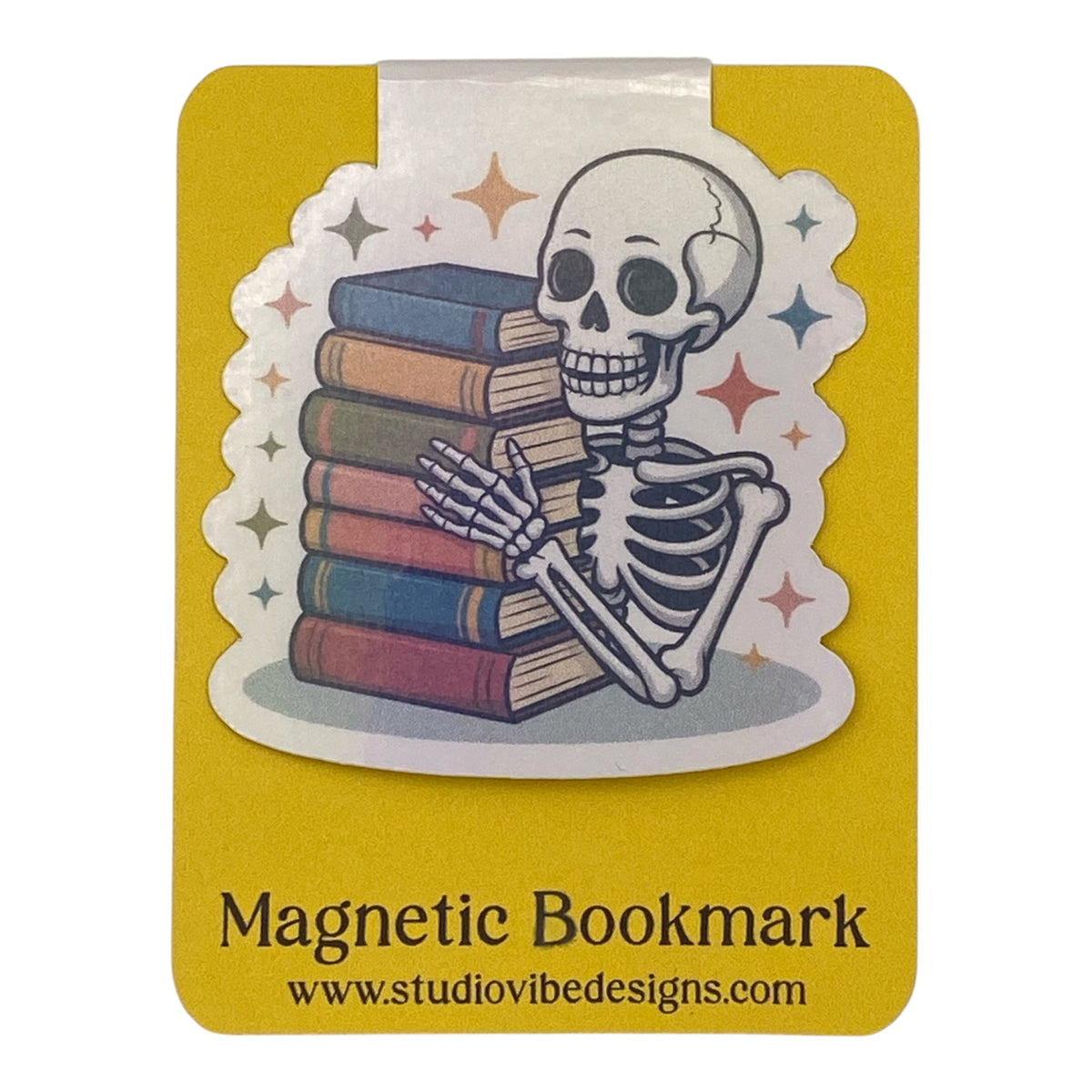 A yellow magnetic bookmark card featuring a die-cut illustration of a cartoon skeleton holding a stack of books, with the text 'Magnetic Bookmark' and 'www.studiovibedesigns.