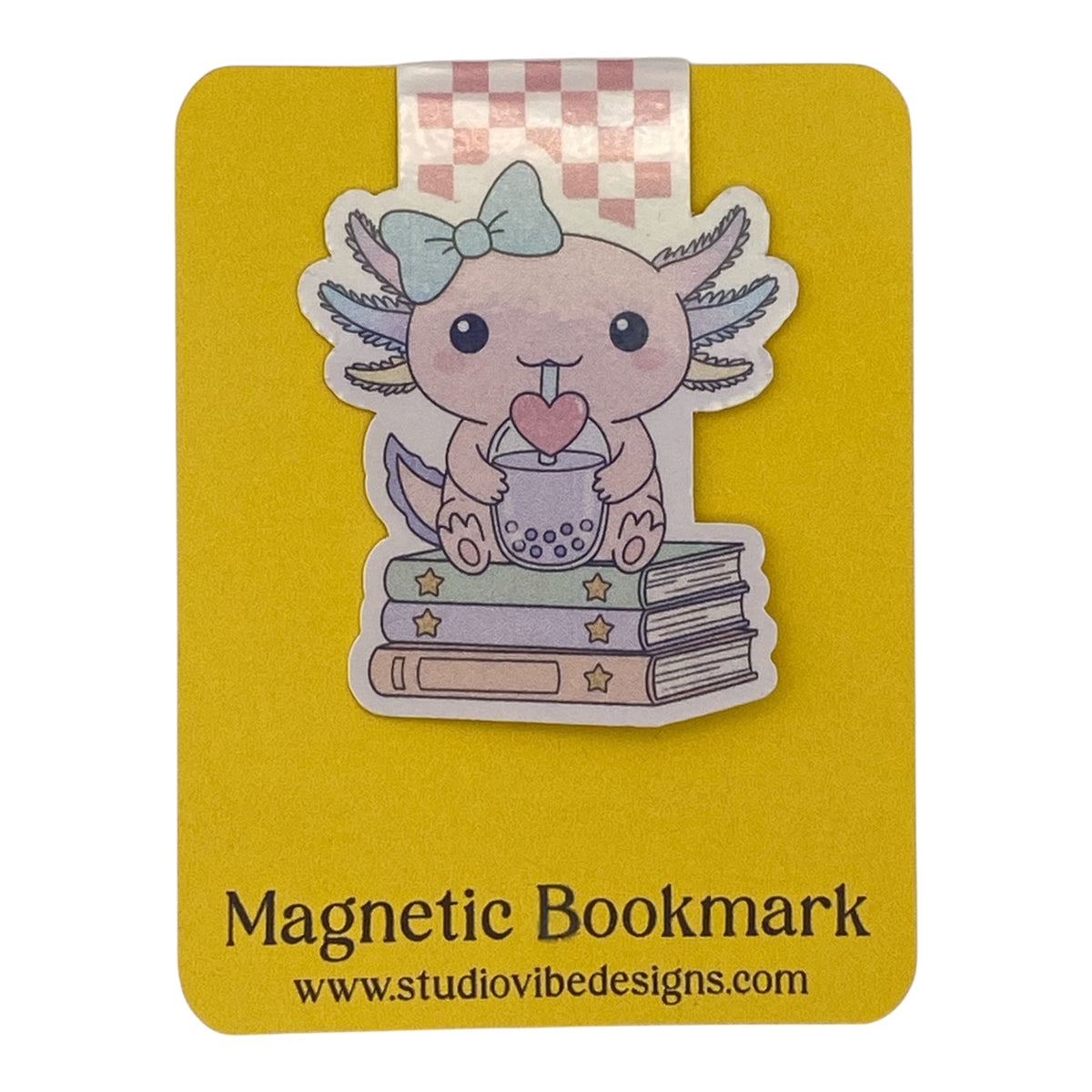 A cute magnetic bookmark of an Axolotl character sitting on books with a pink heart, attached to a yellow magnetic bookmark card that reads 'Magnetic Bookmark' and 'www.studiovibedesigns.