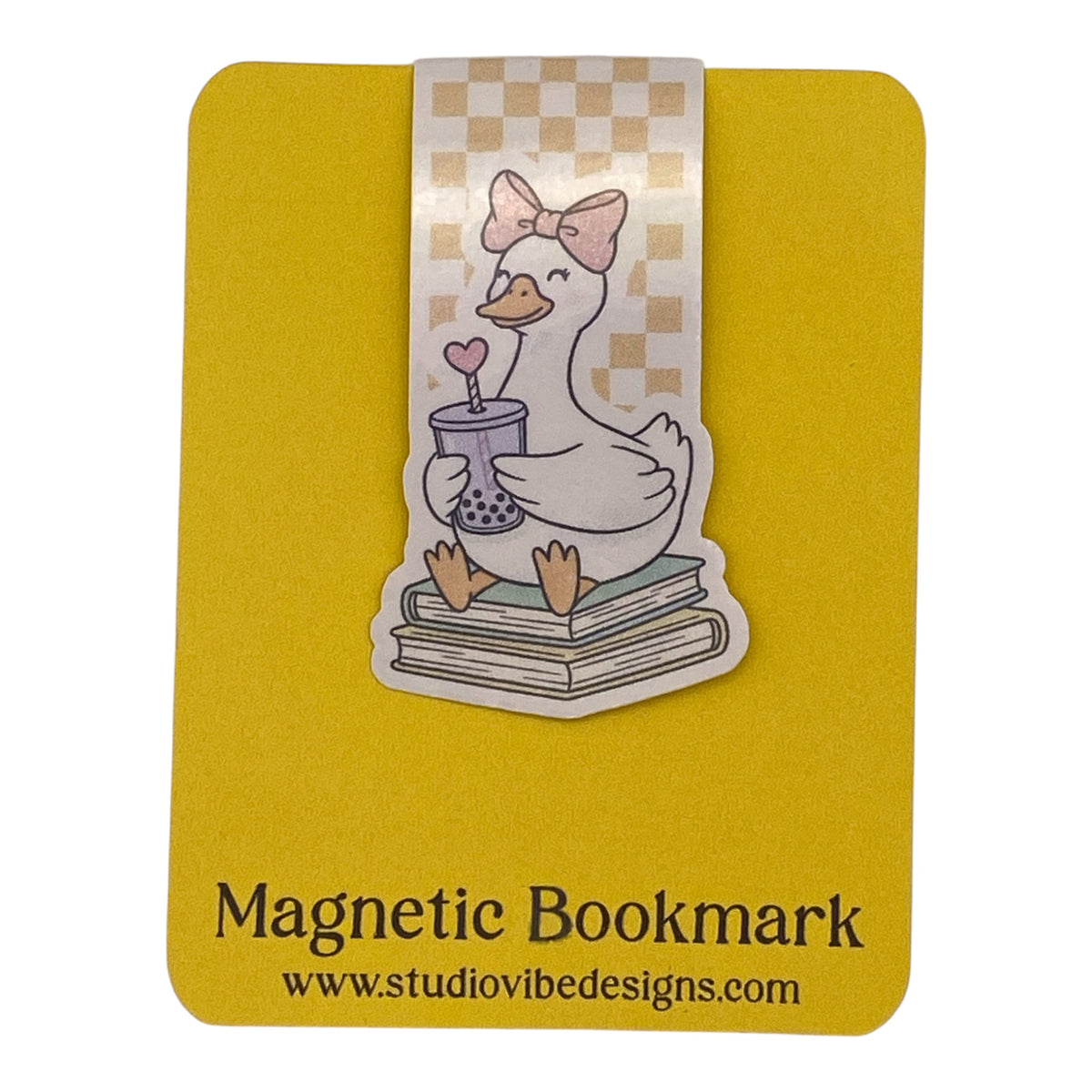 A magnetic bookmark featuring a cute cartoon duck sitting on books and holding a cup, displayed on a yellow backing card with the text 'Magnetic Bookmark' and 'www.studiovidesigns.