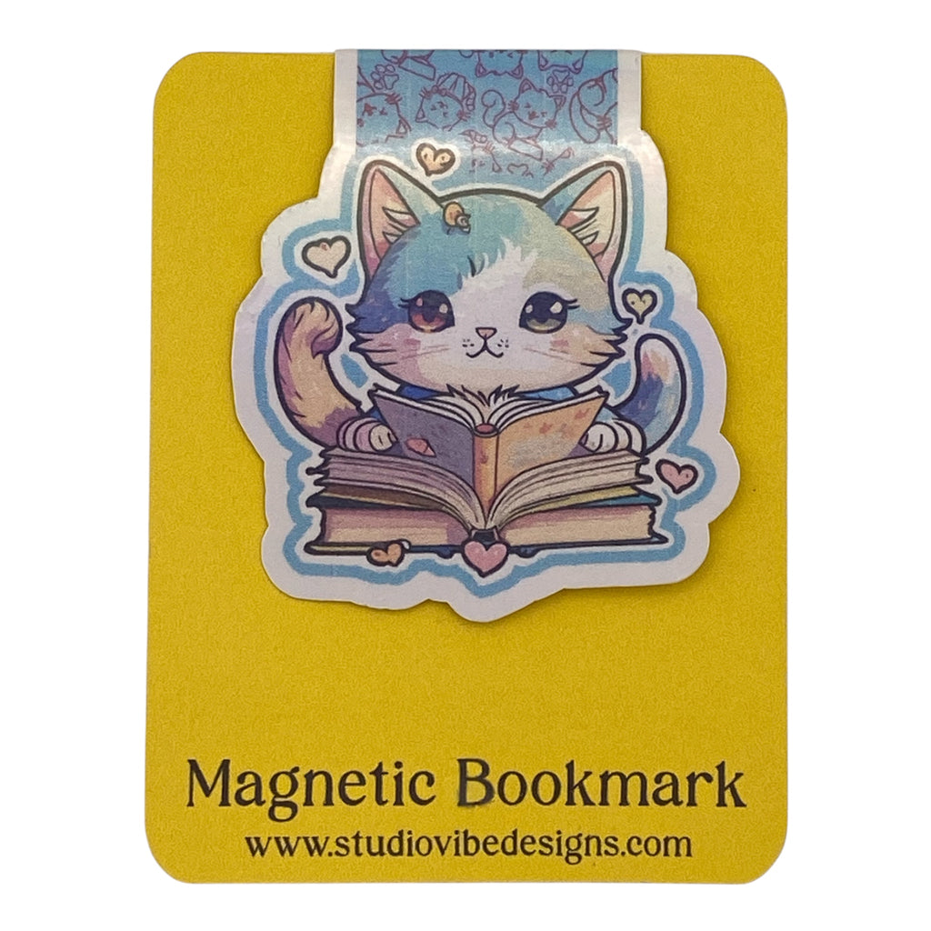 A cute magnetic bookmark of a blue and white cat reading a book, mounted on a yellow backing card labeled 'Magnetic Bookmark' with the website 'www.studiovibedesigns.