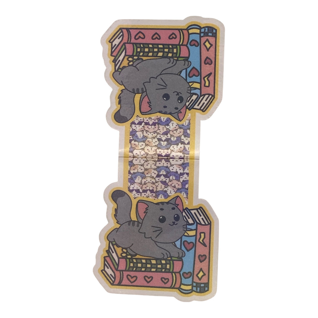 A magnetic bookmark featuring a cute cartoon gray cat lounging on colorful stacks of books, with a purple patterned center section, shown on a plain white background.