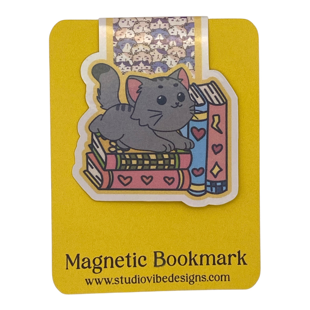 A cute gray cartoon cat magnetic bookmark on a yellow backing card. The bookmark features a gray cat sitting on pink and blue books with hearts.