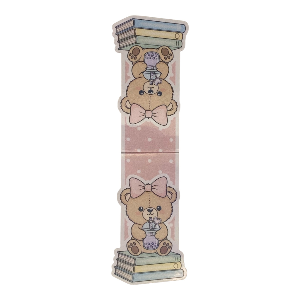 A tall, narrow decorative magnetic bookmark featuring two cute teddy bear illustrations on a pale pink background with white dots. The top bear wears a pink bow and holds a purple teapot balanced on stacked books, while the bottom bear wears a large pink bow and holds a purple teapot balanced on stacked books.