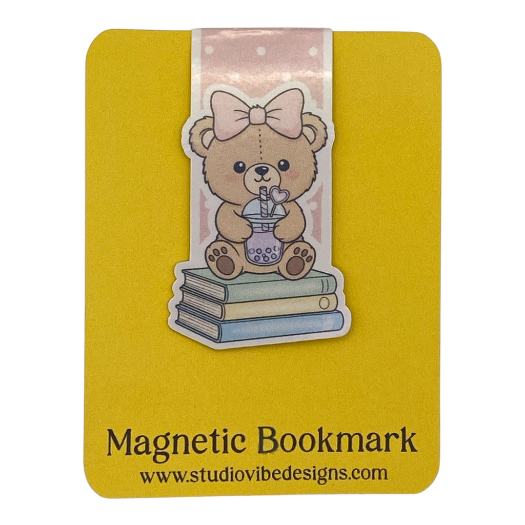 A yellow magnetic bookmark card featuring a cute teddy bear illustration sitting on stacked books with a pink bow, plus the text 'Magnetic Bookmark' and 'www.studiovibedesigns.