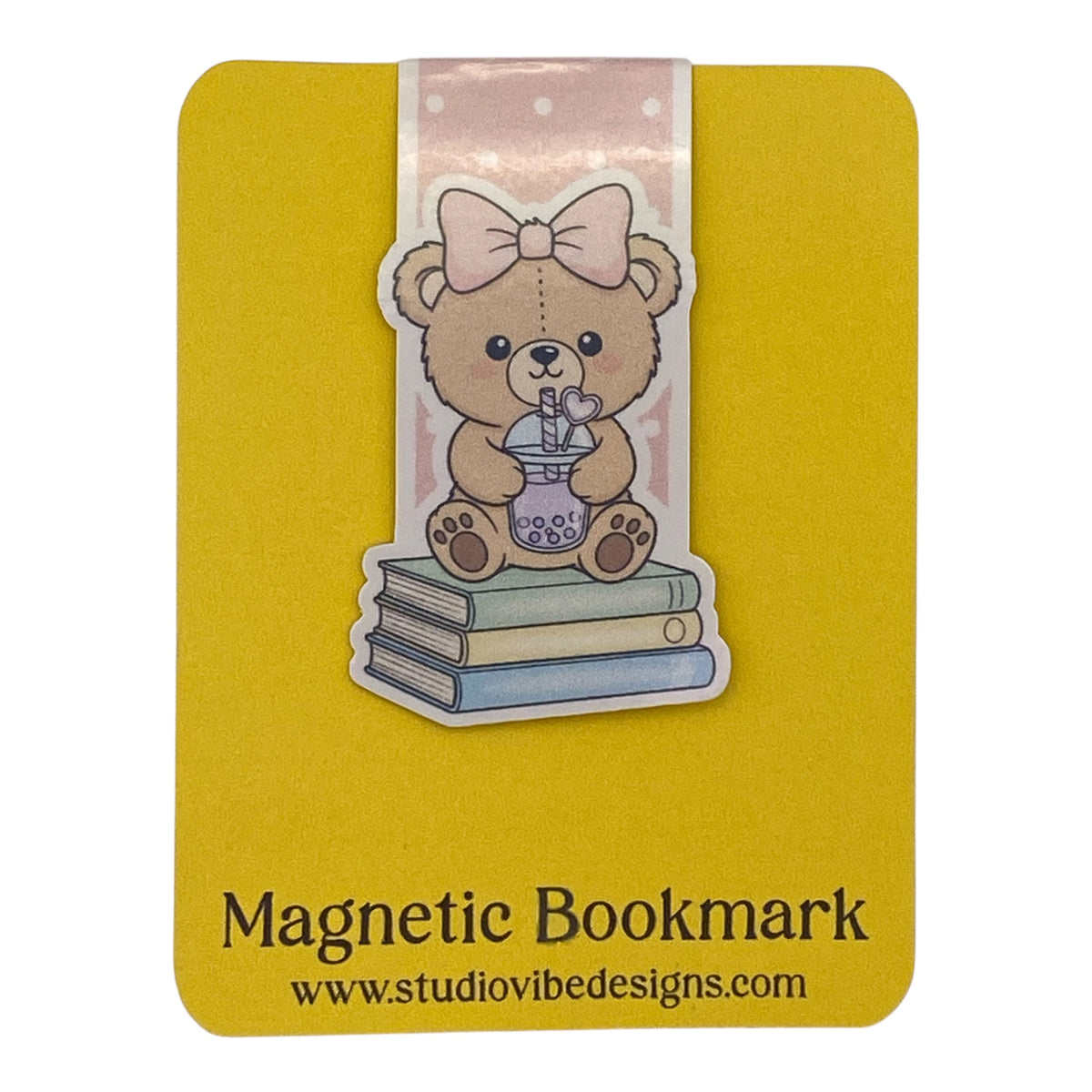 A yellow magnetic bookmark card featuring a cute teddy bear illustration sitting on stacked books with a pink bow, plus the text 'Magnetic Bookmark' and 'www.studiovibedesigns.