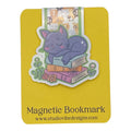 A cute magnetic bookmark of a purple cat sleeping on stacked books, shown on a yellow backing card labeled 'Magnetic Bookmark' with the website www.studiovibedesigns.