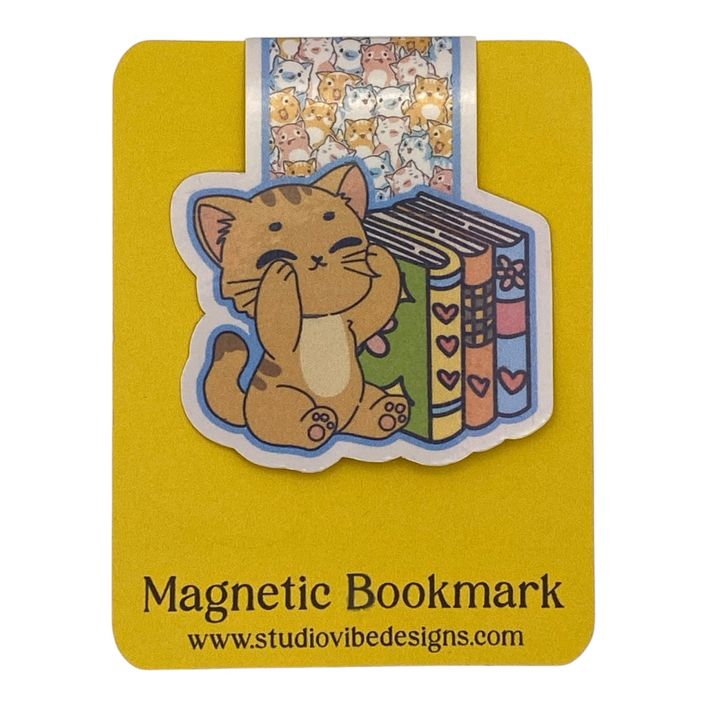 A cute cartoon cat bookmark on a yellow backing card. The sticker shows a brown tabby cat sitting next to colorful books, with a small strip of repeating cat faces above.