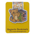 A cute cartoon cat bookmark on a yellow backing card. The sticker shows a brown tabby cat sitting next to colorful books, with a small strip of repeating cat faces above.