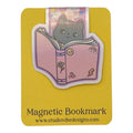A cute die-cut magnetic bookmark featuring an illustration of a gray cat reading a pink book, presented on a yellow backing card with the text 'Magnetic Bookmark' and 'www.studiovibedesigns.