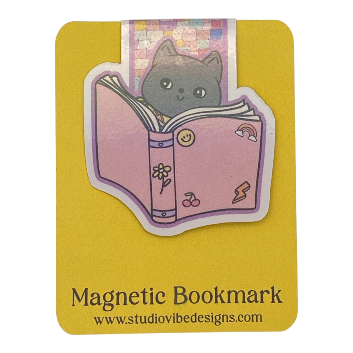A cute die-cut magnetic bookmark featuring an illustration of a gray cat reading a pink book, presented on a yellow backing card with the text 'Magnetic Bookmark' and 'www.studiovibedesigns.