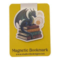 A yellow magnetic bookmark card featuring a die-cut illustration of a blue dragon perched on a stack of old books, with the text 'Magnetic Bookmark' and 'www.studiovidesigns.
