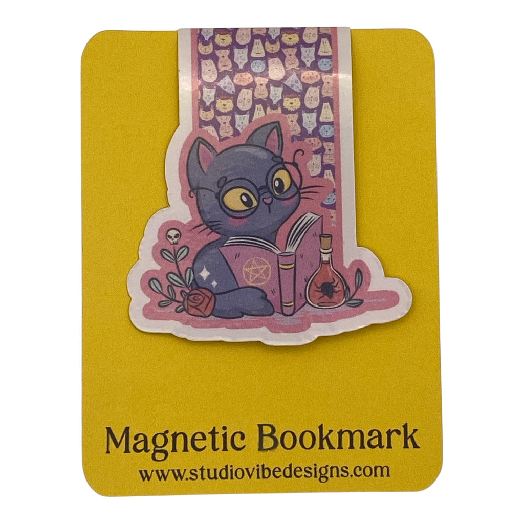 A die-cut magnetic bookmark featuring a purple cat with glasses reading a book, placed on a yellow backing card labeled 'Magnetic Bookmark' with the website www.studiovidesigns.