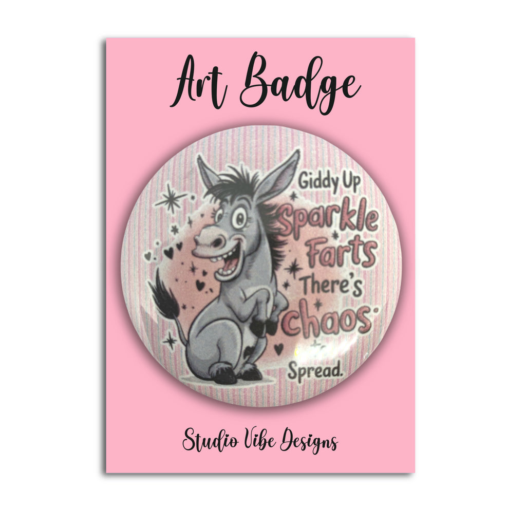 A circular novelty pin badge featuring a cartoon donkey with the text 'Giddy Up Sparkle Farts There's Chaos Spread.' on a pink backing card labeled 'Art Badge' and 'Studio Vibe Designs'.