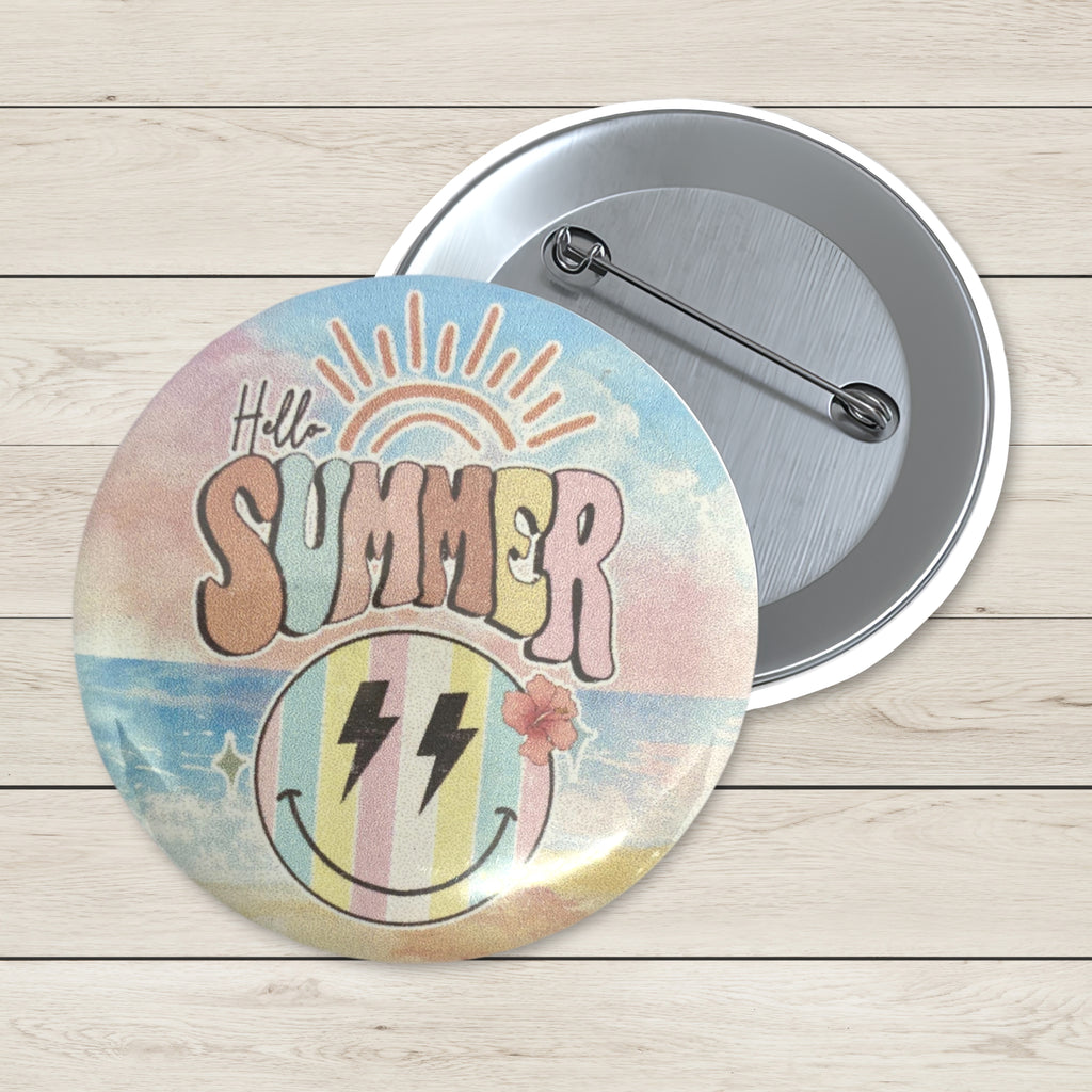 Two round pinback buttons displayed on a light wood background. The front button features a retro summer design with the text 'Hello SUMMER', a sun, and a striped smiley face with lightning bolts.