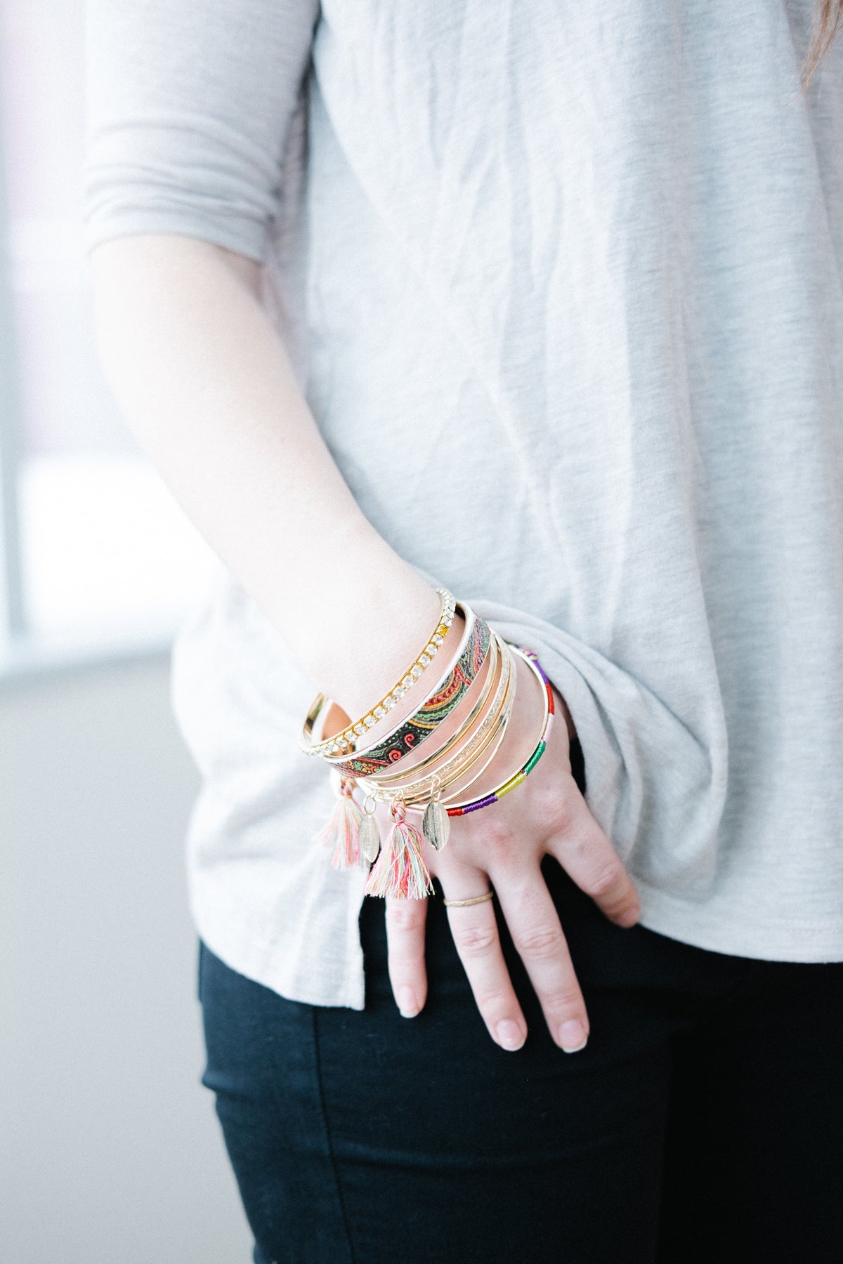 Woman standing with hand in jean pocket-showing lots of metal coloured bracelets on her wrist